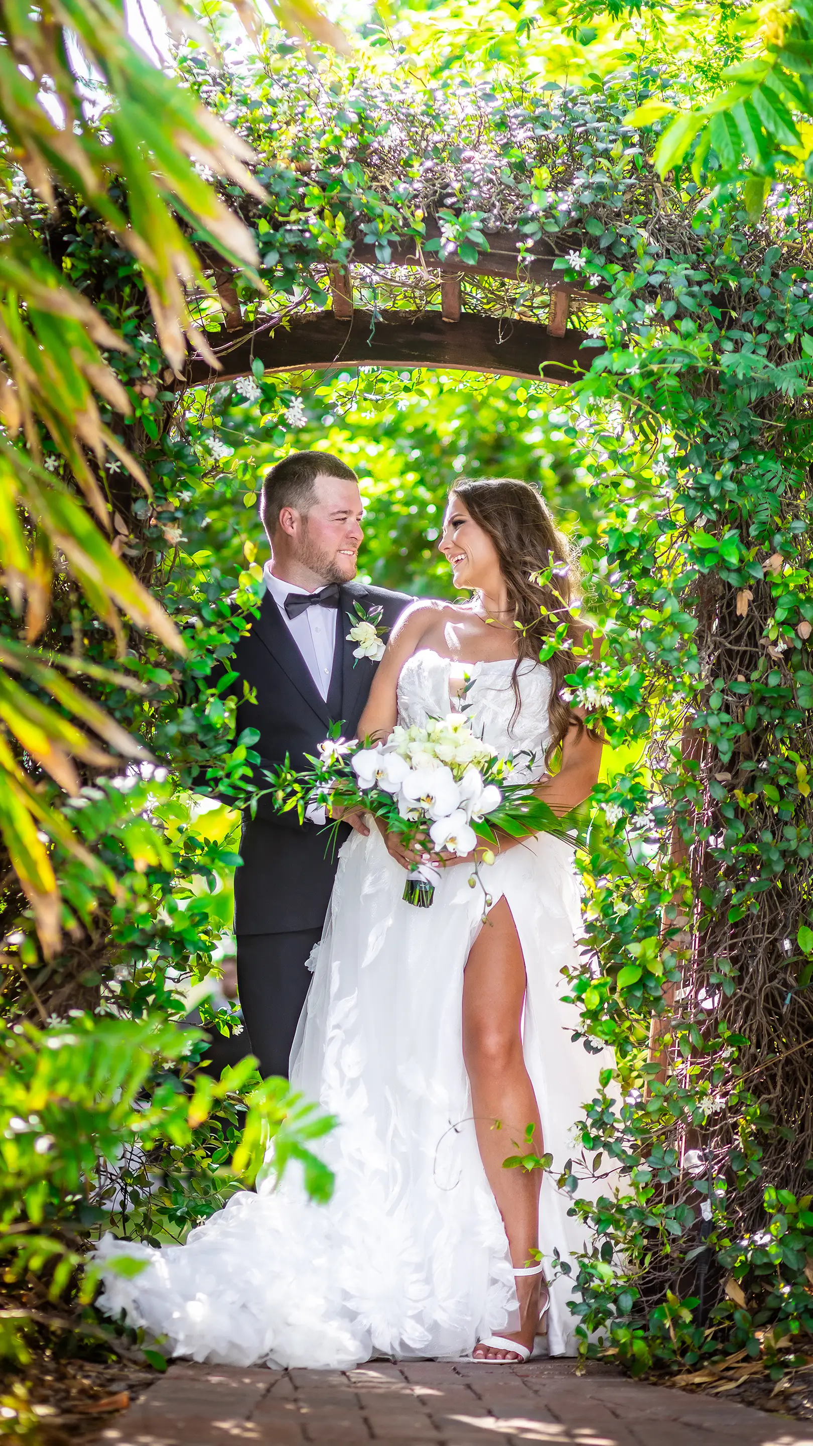 Bride and groom laughing together beneath a vine-covered garden arch